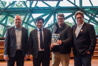 Four men standing together, one holding a book