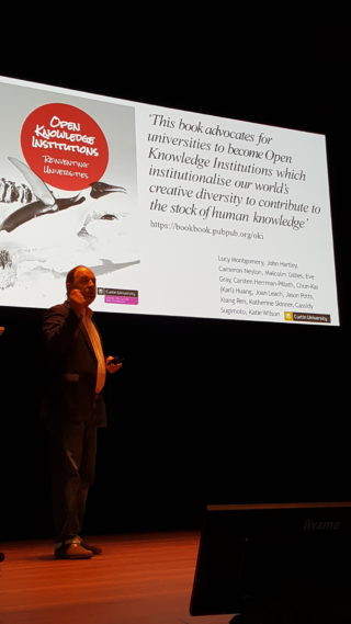 Image of Cameron Neylon presenting a PowerPoint on stage