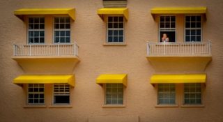 person looking out of apartment window with yellow awnings