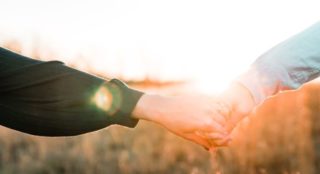 two arms holding hands with the sun shining behind them