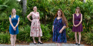 Picture of the four female team members posing in front of green foliage