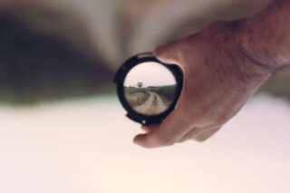 hand holding a camera lens with country lane image in the lens