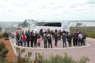 Group of around 40 people outdoors forming a large circle with a white bus in the background