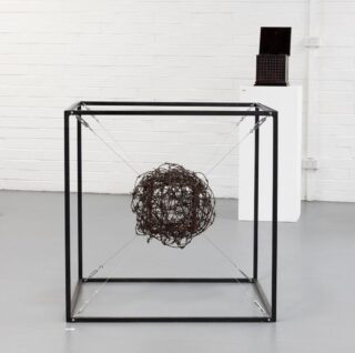A cube shape box with no sides and a mass of wire in a ball shape suspended with metal wires in the centre