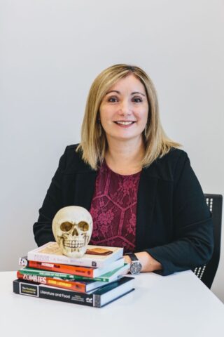 Picture of Lorna with a small pile of books in front of her with a skull on the top