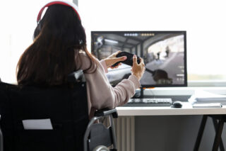 Cover of the book - looking over the shoulder of a girl holding a game controller in a wheelchair facing a screen