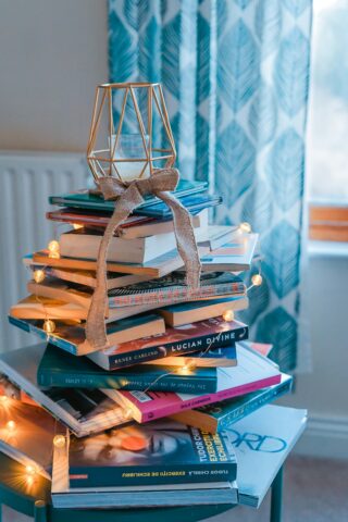 Brown wooden frame candle holder and fairy lights on top of an untidy pile of books